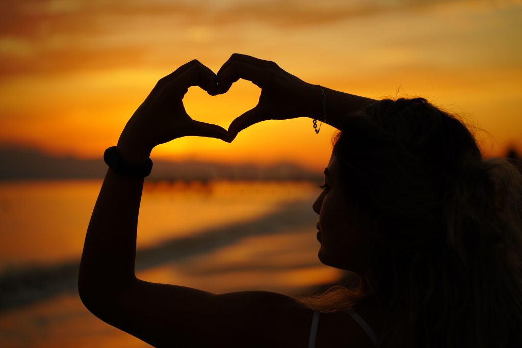 Silhouette of a woman making heart shape with hands against a vivid Antalya beach sunset.